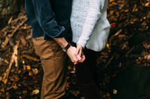 torso of a couple holding hands in fall leaves 