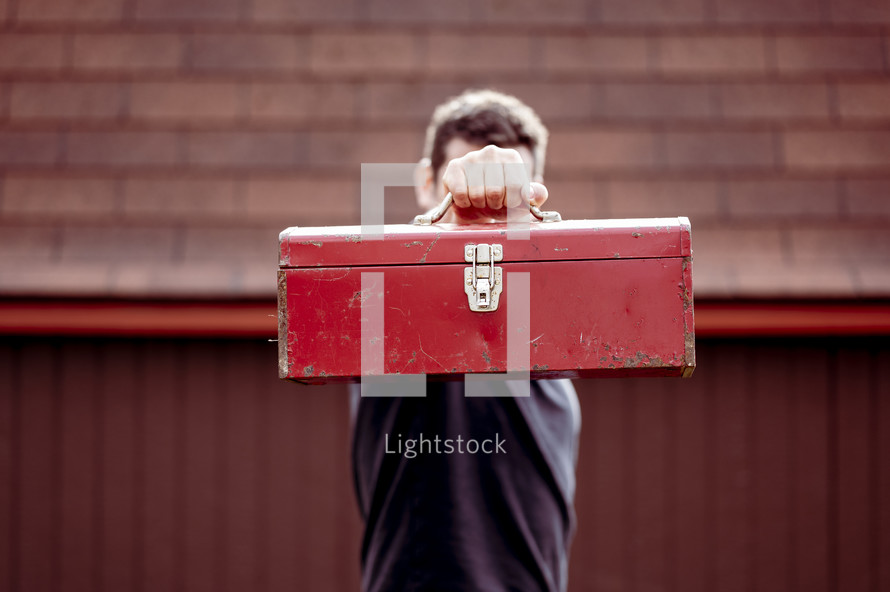 a man standing outdoors holding a red toolbox 