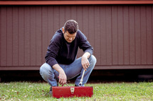 a man standing outdoors going through a red toolbox 