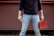 a man standing outdoors holding a red toolbox 