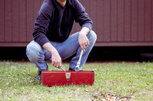 a man standing outdoors going through a red toolbox 