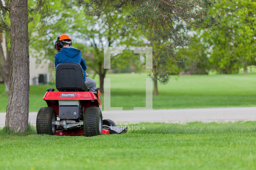 a boy child cutting the grass on a riding lawn mover 