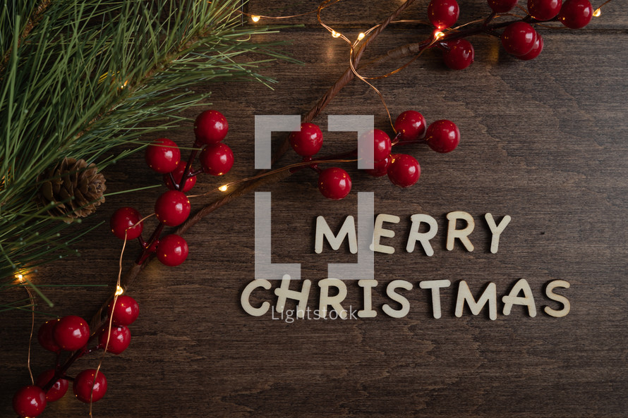 red berries and fairy lights on a wood background and words Merry Christmas 