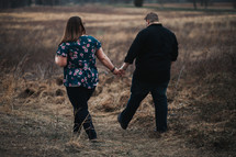a couple walking through a brown field 