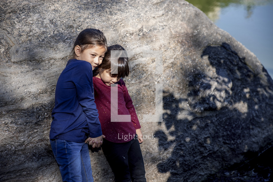 Little girls holding hands in front of a rock