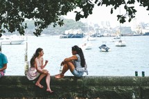 women sitting on a wall in conversation near a harbor 