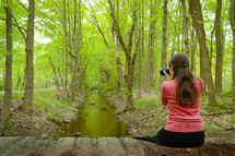 girl with a camera taking a picture in a forest 