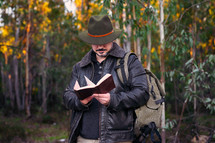 Mature man with hat and jacket reading an old book 
