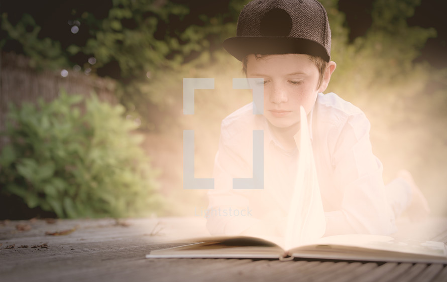 a boy child reading outdoors turning the glowing pages of a book 