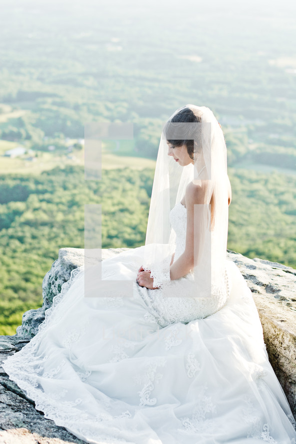 a bride sitting at the edge of a mountain cliff 