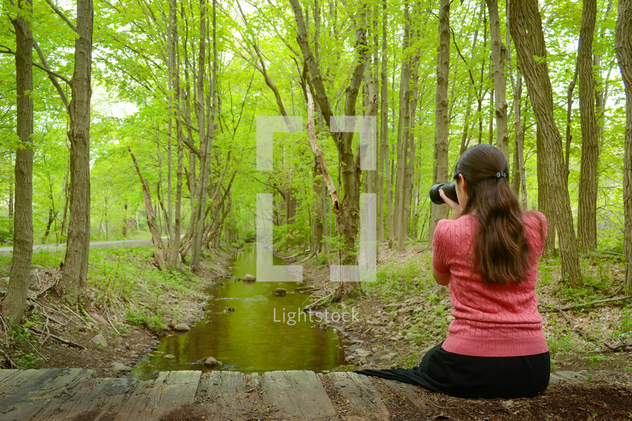 girl with a camera taking a picture in a forest 