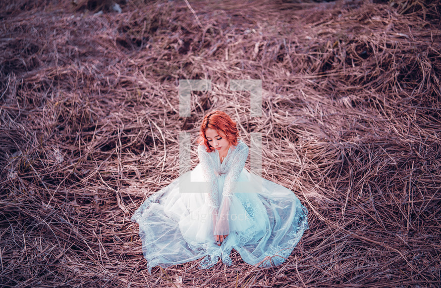 a woman sitting in a field in a long dress