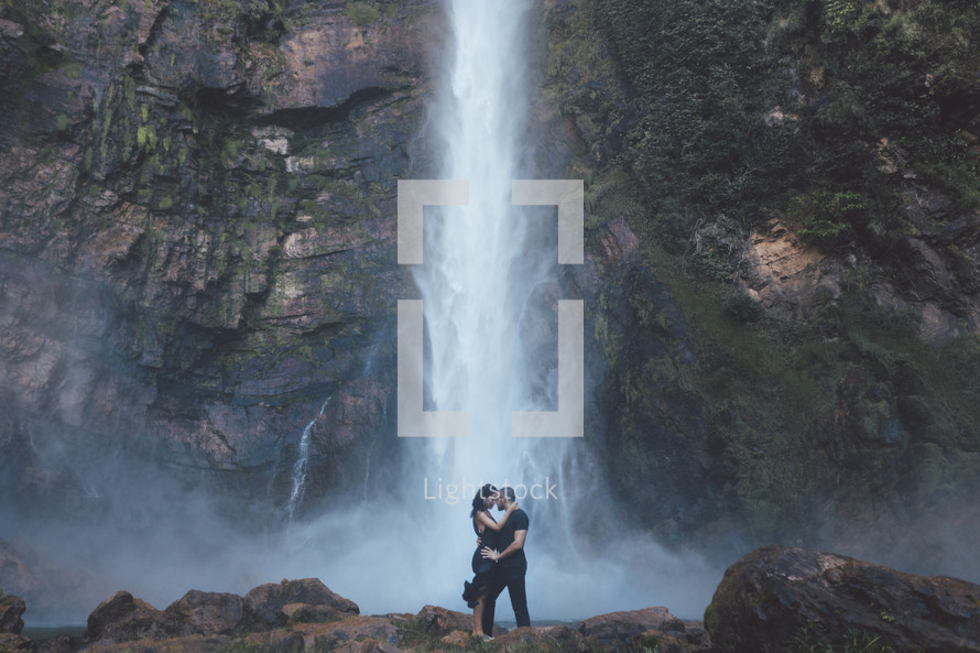 a couple holding each other in front of a waterfall 