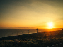 A brilliant sunset shines on wind turbines in the countryside.