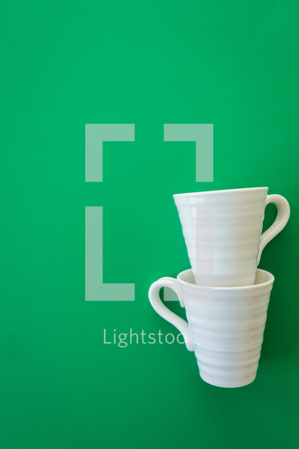 stacked white mugs on a green background 