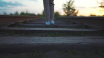 Refugee concept. Lonely woman walking on the rail track at sunset time. Low angle view of the legs. Young woman wearing white sneakers walking along the railroad tracks.