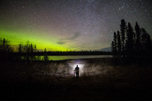 a man standing under the night sky and an aurora 