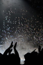 silhouettes of clapping hands under bubbles at a concert 