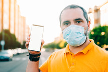 Portrait of 40s aged man with surgical medical mask standing, holding and showing smart phone display. medicine and health care concept.