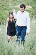 A man and woman walking hand-in-hand through tall grass.