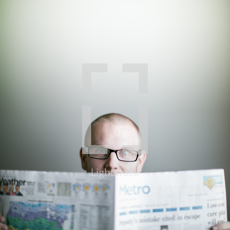 man wearing glasses reading the newspaper amazed by a story of Good news