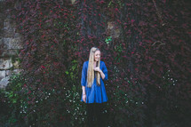 blonde woman standing in front of an ivy covered wall 