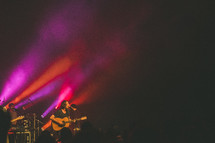 man with a guitar singing into a microphone on stage and pink strobe lights 