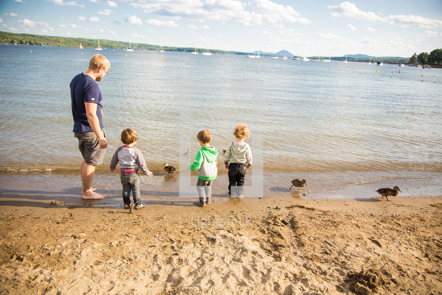children playing with ducks on a lake shore beach