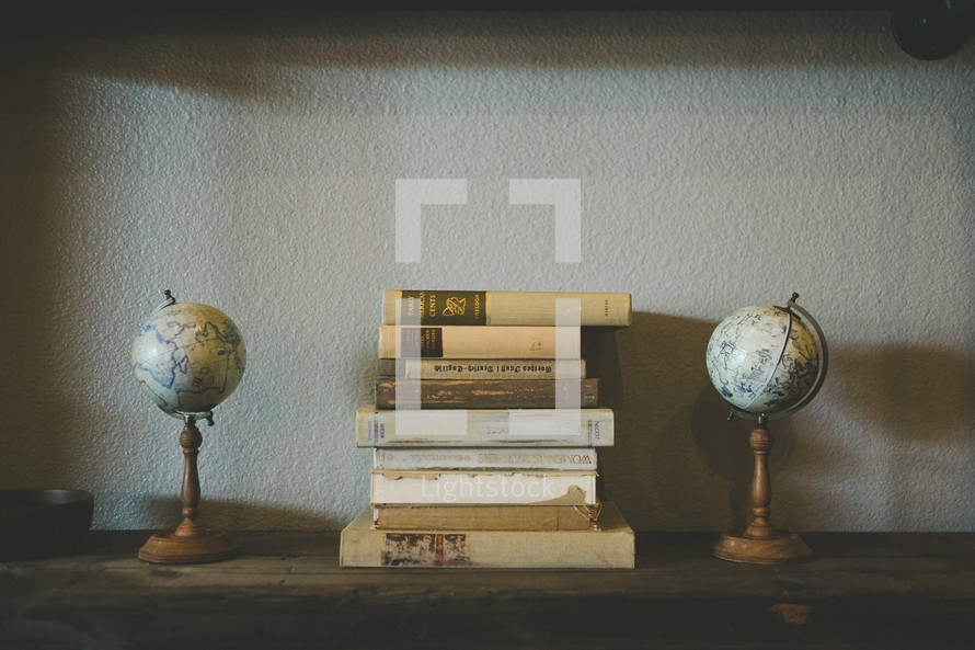 A stack of books between two globes on a wooden shelf.