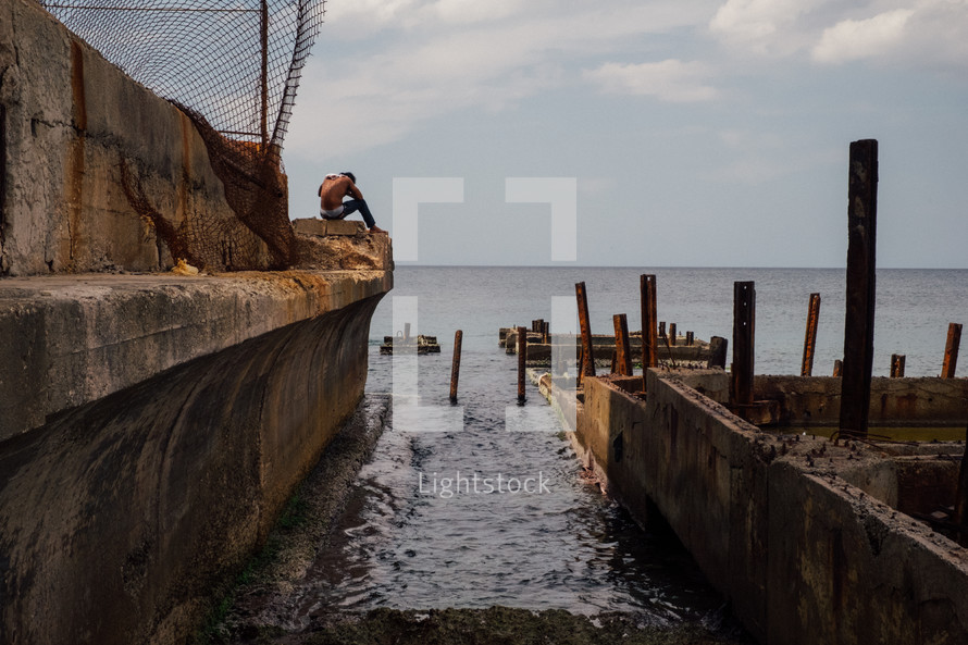 man sitting on a concrete wall along the shore in Cuba 