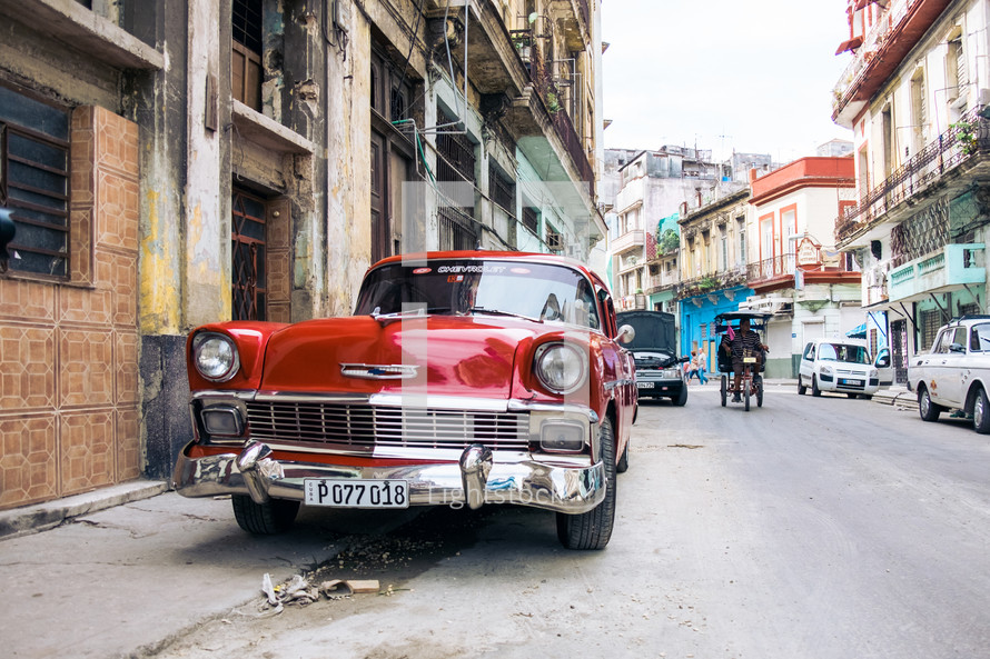 Side street in Downtown Havana, Cuba, an antique car sits on the side of the road as a horse and buggy prepare to pass