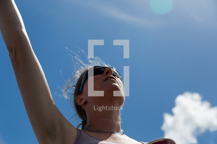 woman with a raised hand standing under a blue sky 