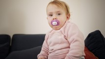 Cute baby girl playing at home with a pacifier in her mouth