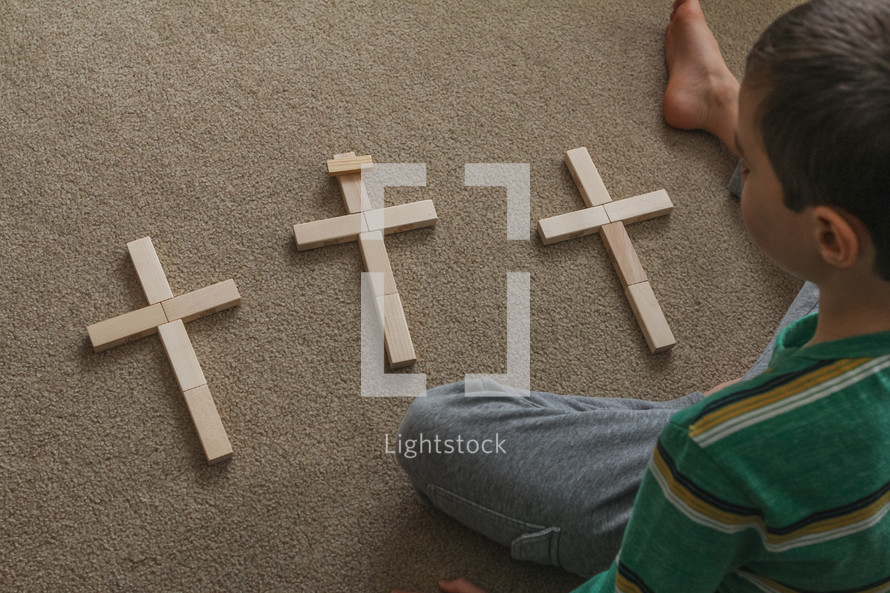 a child playing with crosses made of wooden blocks on carpet 