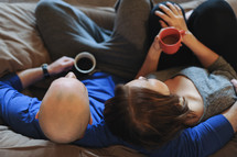 a couple snuggling on a couch holding coffee mugs 