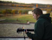 young woman sitting on a porch playing a guitar 