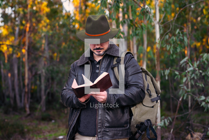 Mature man with hat and jacket reading an old book 