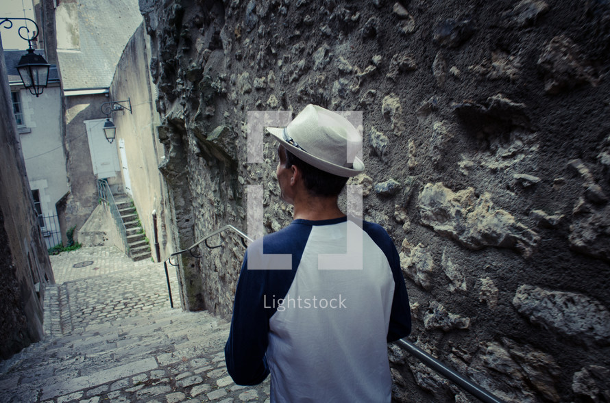 A man with a hat walks down some stone steps in an old town