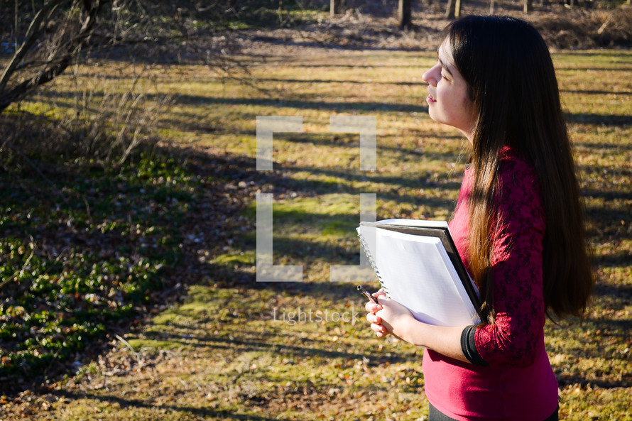 a girl standing in warm sunlight holding a notebook 