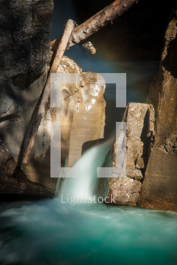 Bright waterfall rushing between rocks and branches slow shutter speed