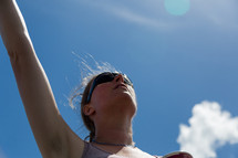 woman with a raised hand standing under a blue sky 