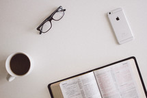 open Bible, coffee mug, reading glasses, and iPhone 