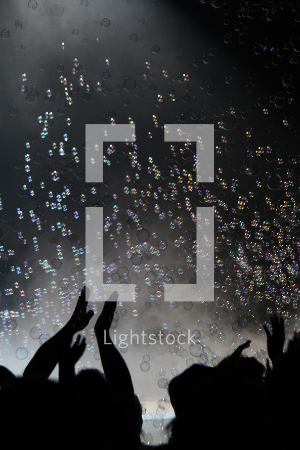 silhouettes of clapping hands under bubbles at a concert 