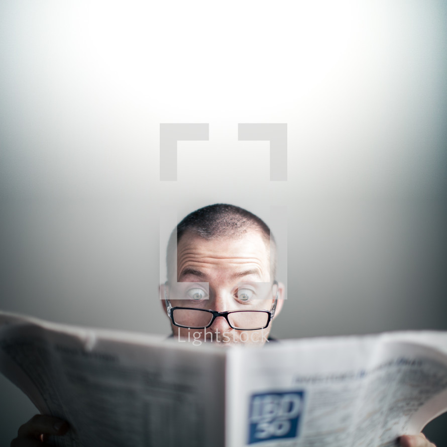 man wearing glasses reading the newspaper amazed by a story of Good news