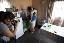 Photographer capturing an African woman cooking in her home with a baby on her back.