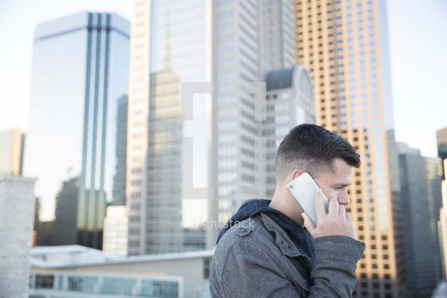 a man talking on a cellphone surrounded by city buildings 