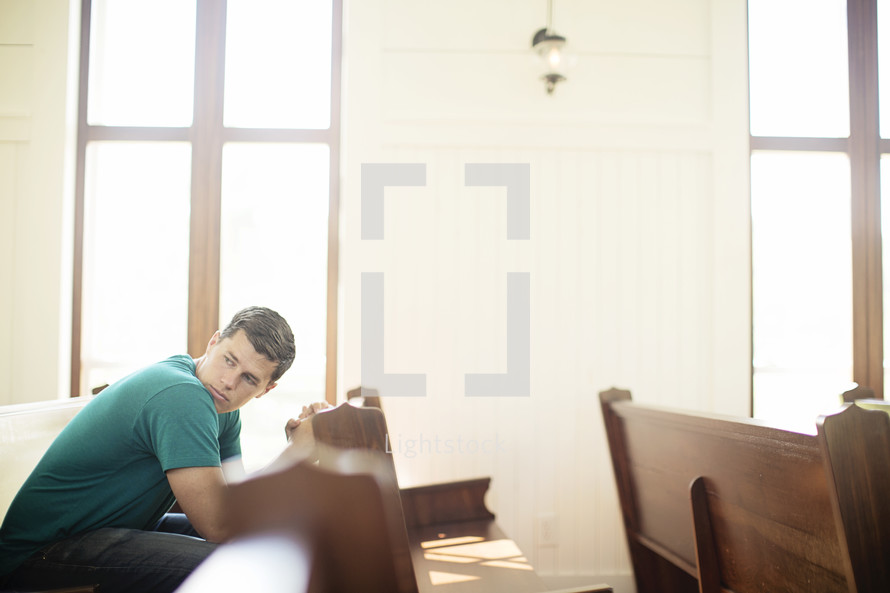 Man looking over his shoulder while praying in a church pew.