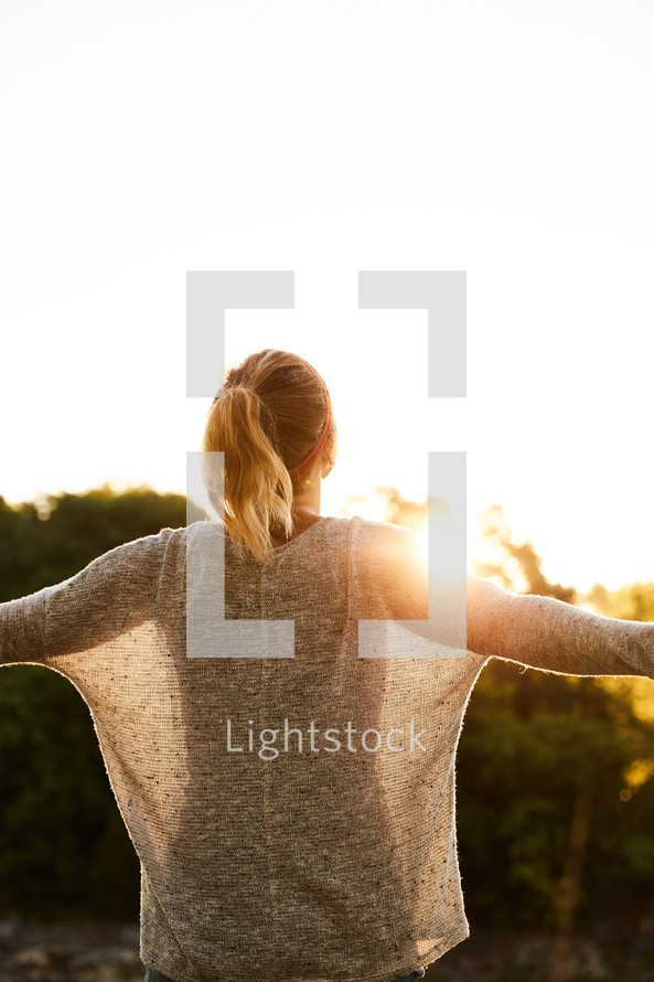 a woman standing outdoors at sunset with outstretched arms 