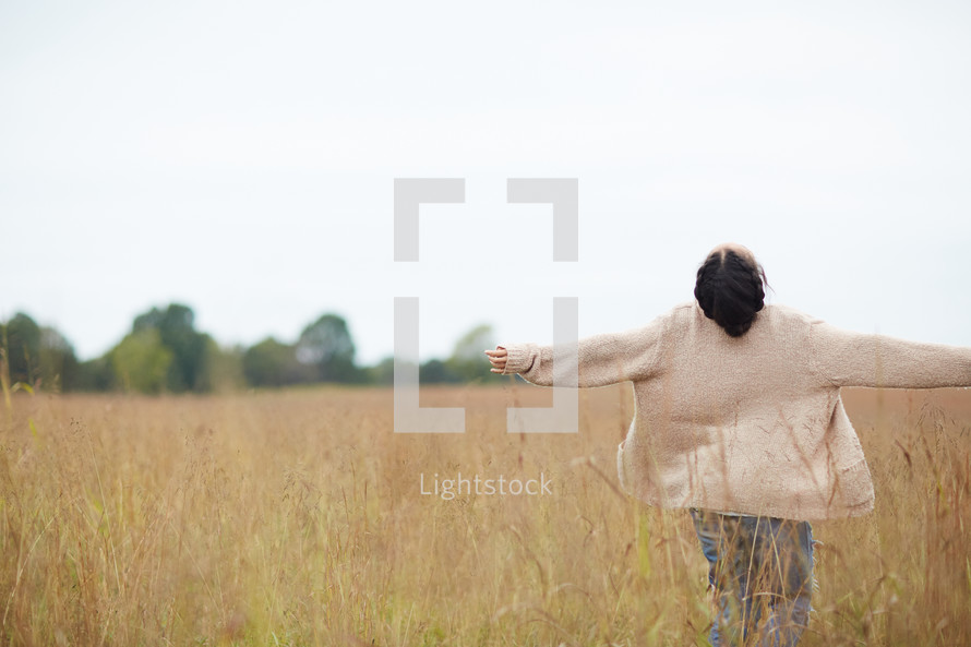 a woman with open arms walking through a field 