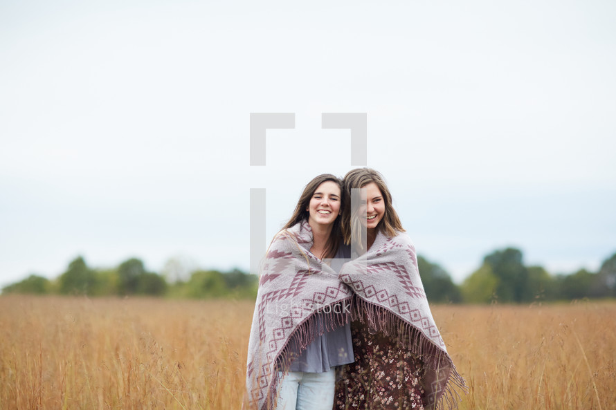 friends wrapped in a blanket standing in a field 